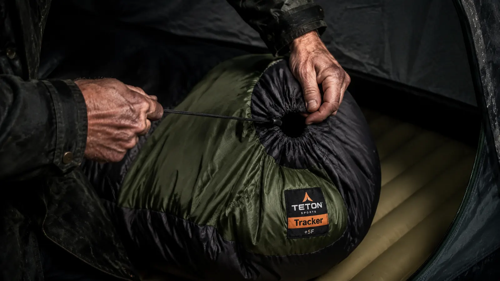 Person zipping up a mummy sleeping bag inside a tent at night