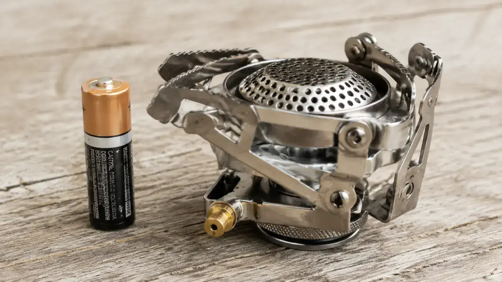 Side-by-side size comparison of a BRS-3000T stove next to a AA battery, both on a wooden camp table