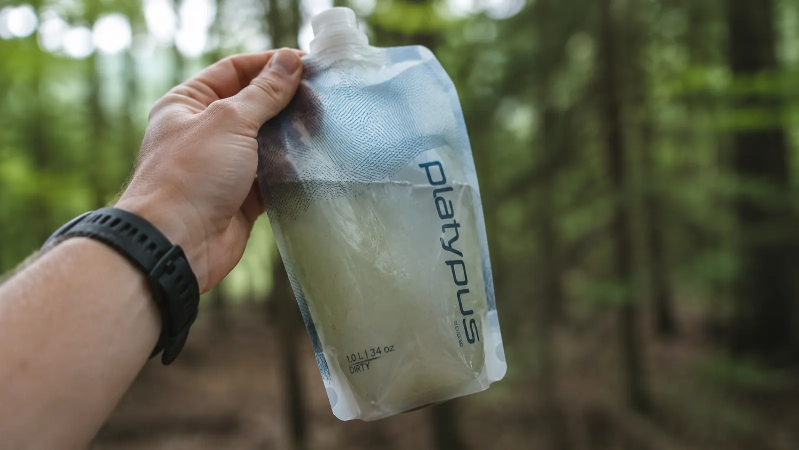 Close-up of murky glacial sediment in a clear soft flask beside a stream, illustrating turbid water before filtering