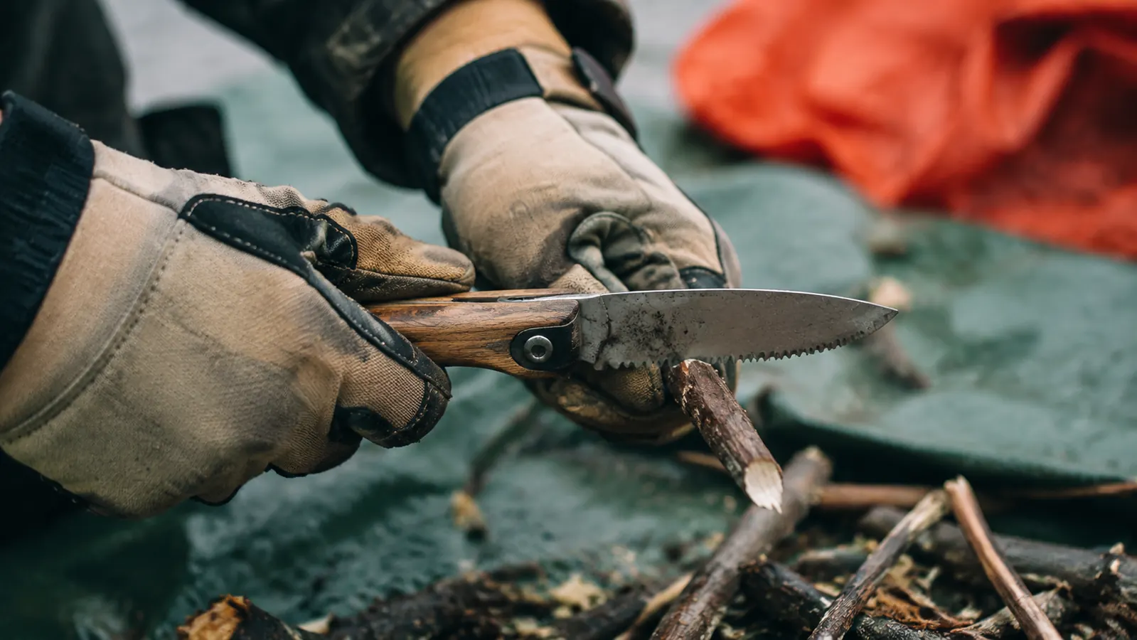 Hands using a multi-tool saw blade to notch a small branch while building a field repair for a broken tent pole